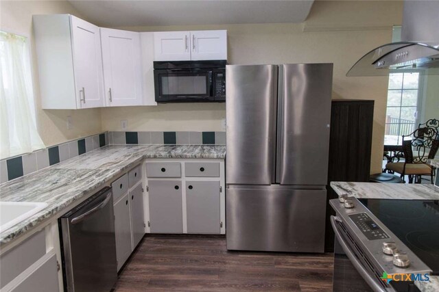 kitchen featuring stainless steel appliances, light stone counters, range hood, white cabinets, and dark hardwood / wood-style flooring