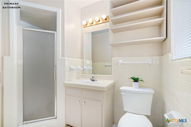 bathroom with a shower with door, vanity, tile walls, and toilet