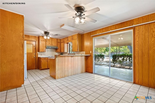 kitchen with white fridge, kitchen peninsula, ceiling fan, and wood walls