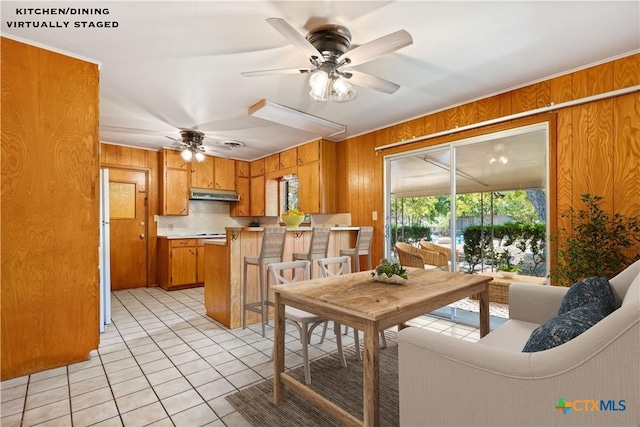 tiled dining space featuring ceiling fan and wood walls