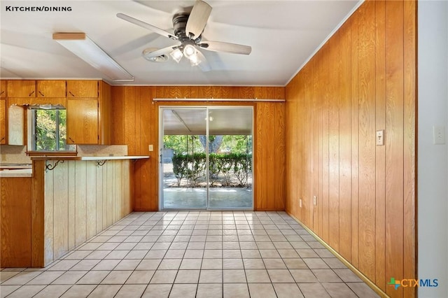 kitchen with ceiling fan, wood walls, light tile patterned floors, and a wealth of natural light