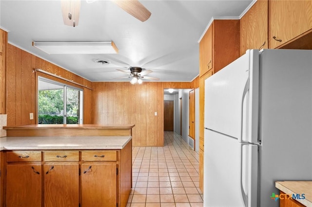 kitchen with light tile patterned floors, wooden walls, ceiling fan, and white refrigerator