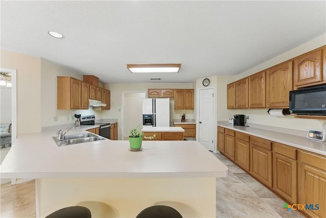 1233 Oakcrest Dr, Pleasanton, TX 78064 - kitchen featuring white refrigerator with ice dispenser, black microwave, stainless steel electric range oven, under cabinet range hood, and a breakfast bar