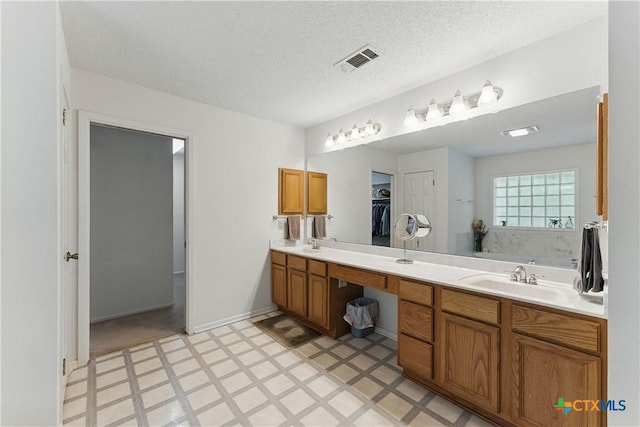 1233 Oakcrest Dr, Pleasanton, TX 78064 - bathroom featuring tile patterned floors, double vanity, a textured ceiling, and a walk in closet