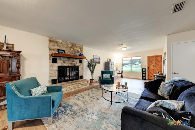 living room with visible vents, a stone fireplace, and wood finished floors