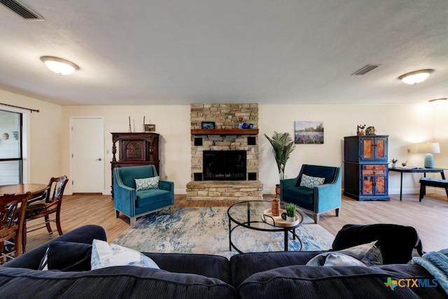 living area with a stone fireplace, light wood-style floors, visible vents, and baseboards