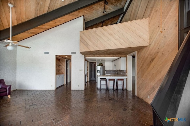 1809 W Harrison Ave, Port Oconnor, TX 77982 - unfurnished living room featuring a towering ceiling, a ceiling fan, wood walls, and brick patterned flooring