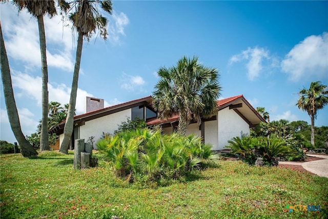 1809 W Harrison Ave, Port Oconnor, TX 77982 - view of property exterior with stucco siding, a chimney, and a lawn