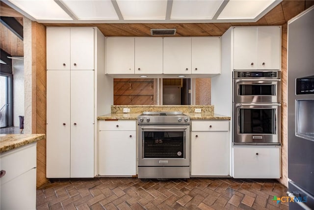 1809 W Harrison Ave, Port Oconnor, TX 77982 - kitchen featuring stainless steel appliances, white cabinetry, light stone counters, and brick patterned floors