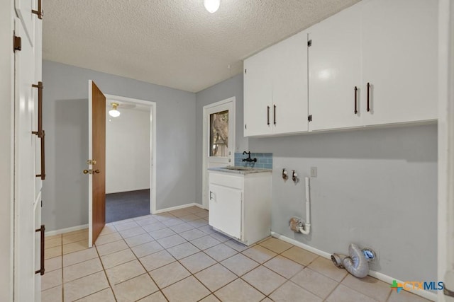 laundry room with sink, light tile patterned floors, cabinets, and a textured ceiling