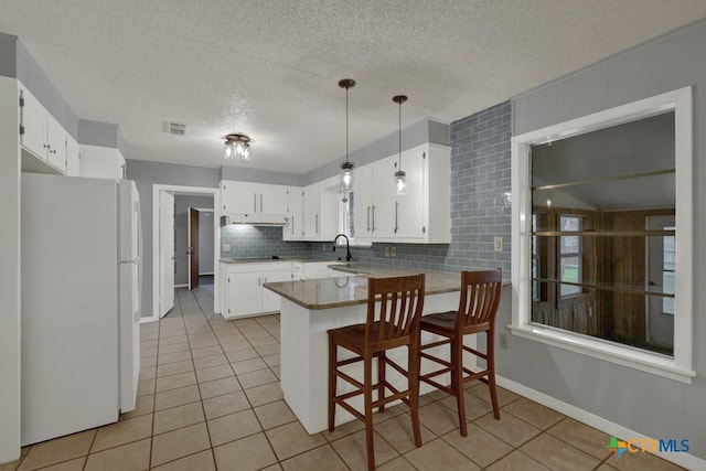 kitchen featuring backsplash, white cabinets, a kitchen bar, white refrigerator, and kitchen peninsula