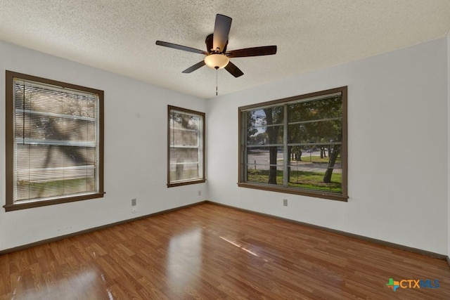 empty room with ceiling fan, plenty of natural light, hardwood / wood-style floors, and a textured ceiling