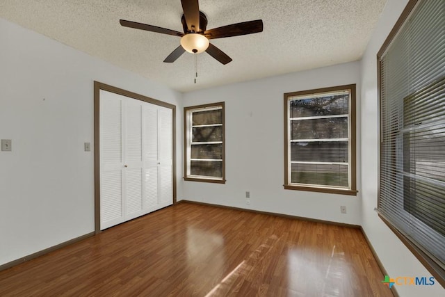 unfurnished bedroom featuring ceiling fan, a closet, wood-type flooring, and a textured ceiling