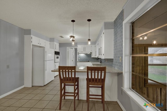 kitchen featuring white appliances, kitchen peninsula, white cabinets, and light tile patterned flooring