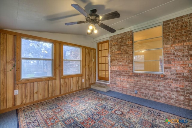 unfurnished room featuring wood walls, ceiling fan, and brick wall