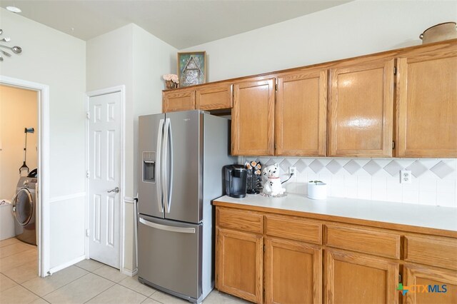 kitchen featuring washer / dryer, stainless steel fridge, light tile patterned floors, and tasteful backsplash