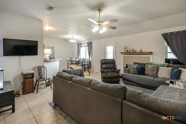 living room with a tiled fireplace, light tile patterned floors, and ceiling fan