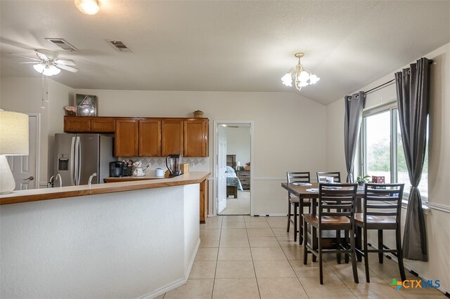 kitchen with ceiling fan with notable chandelier, light tile patterned floors, decorative light fixtures, stainless steel fridge, and vaulted ceiling