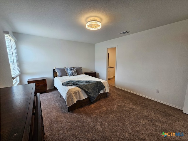 bedroom with dark colored carpet, a textured ceiling, and ensuite bath