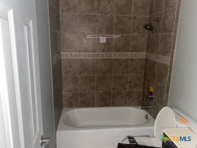 bathroom featuring tiled shower / bath combo and toilet