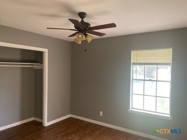 unfurnished bedroom featuring dark wood-type flooring, a closet, and ceiling fan