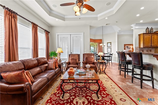 living room featuring ceiling fan with notable chandelier, a tray ceiling, and ornamental molding