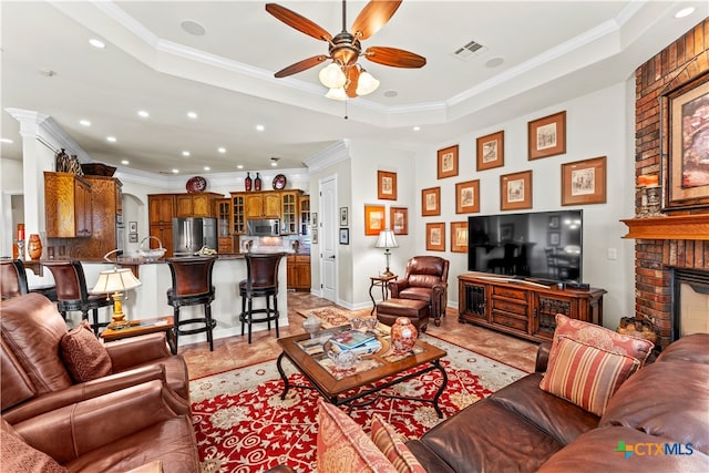 tiled living room featuring a brick fireplace, crown molding, and a tray ceiling