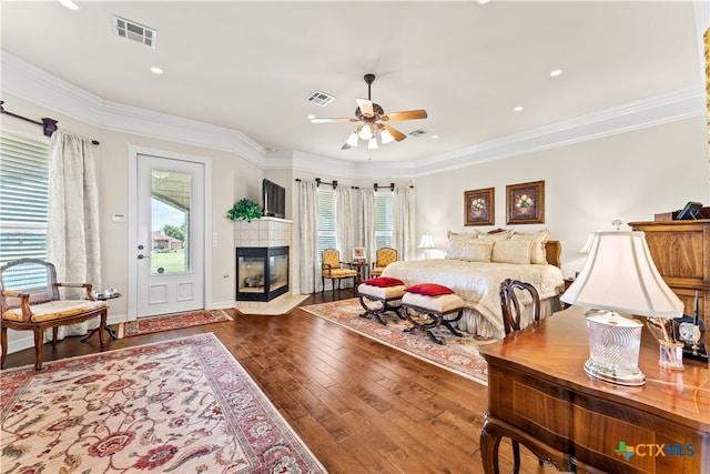 bedroom with ornamental molding, a tiled fireplace, wood-type flooring, and multiple windows