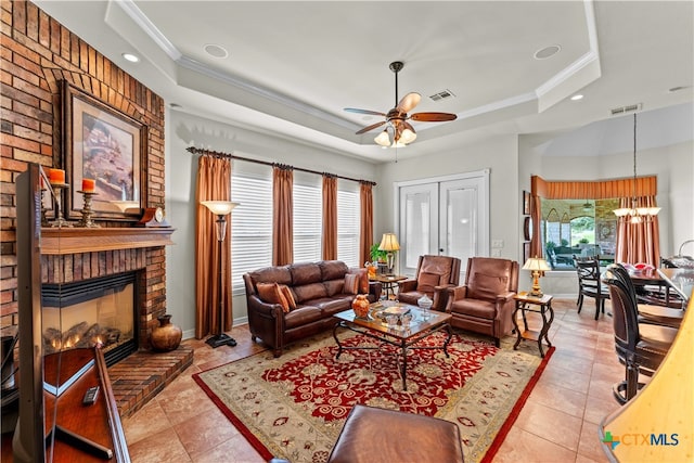 living room featuring light tile patterned flooring, ceiling fan with notable chandelier, a fireplace, a raised ceiling, and crown molding