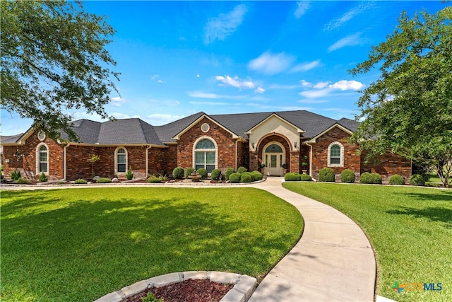 view of front of property featuring a shingled roof, a front yard, and brick siding