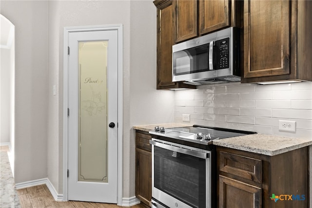 kitchen with stainless steel appliances, dark brown cabinets, light wood-style flooring, and decorative backsplash