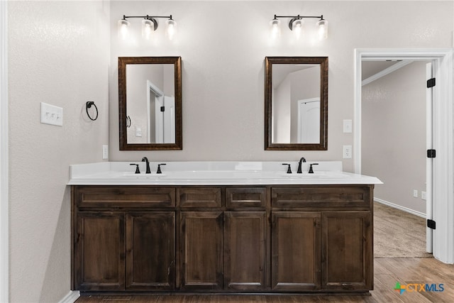 full bath with double vanity, wood finished floors, a sink, and baseboards