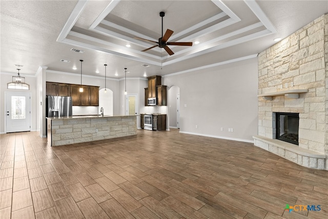 unfurnished living room featuring a tray ceiling, a stone fireplace, arched walkways, and wood finished floors