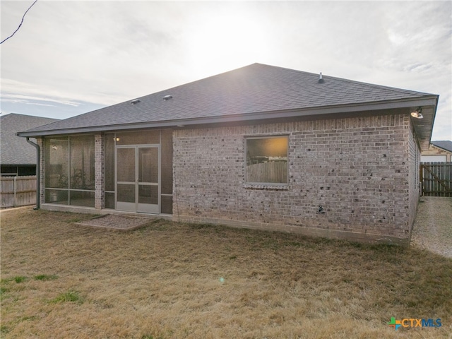 back of house featuring a shingled roof, a sunroom, brick siding, and fence