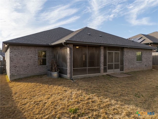 back of property with a shingled roof, a sunroom, brick siding, and a yard