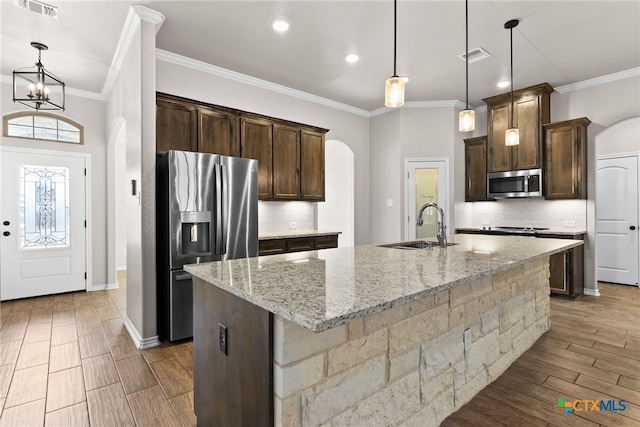 kitchen with arched walkways, stainless steel appliances, backsplash, a sink, and dark brown cabinets