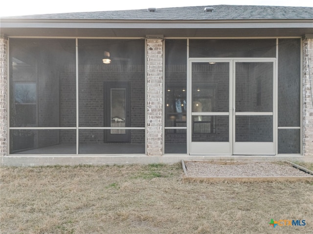 exterior space with a sunroom, a shingled roof, and brick siding