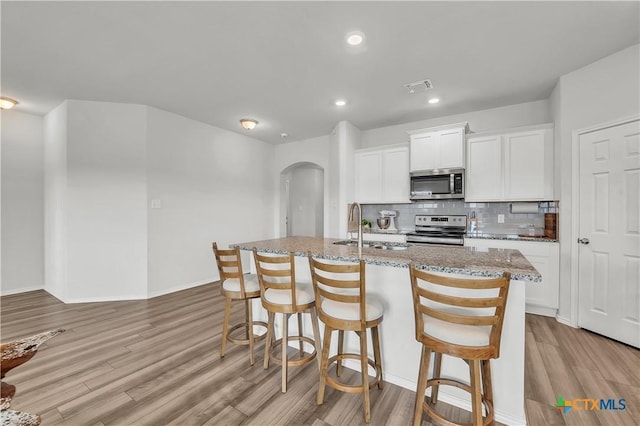 2026 Bee Creek Loop, Copperas Cove, TX 76522 - kitchen featuring appliances with stainless steel finishes, arched walkways, light stone countertops, light wood-style flooring, and tasteful backsplash