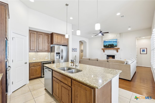 kitchen featuring a large fireplace, light tile patterned flooring, arched walkways, stainless steel appliances, and a sink