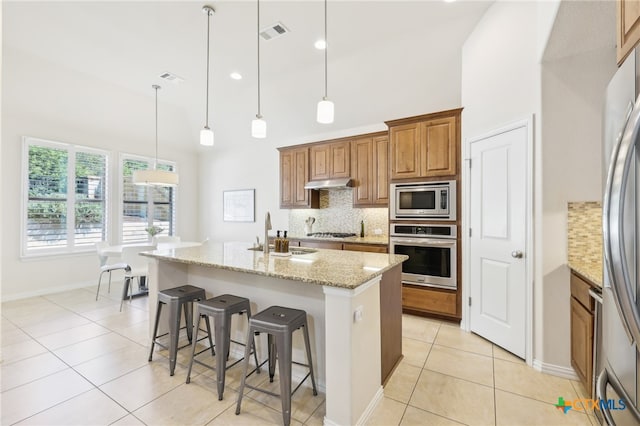 kitchen with visible vents, a sink, stainless steel appliances, under cabinet range hood, and brown cabinets