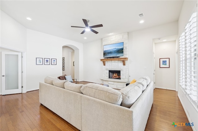 living area featuring visible vents, a ceiling fan, hardwood / wood-style flooring, arched walkways, and a fireplace