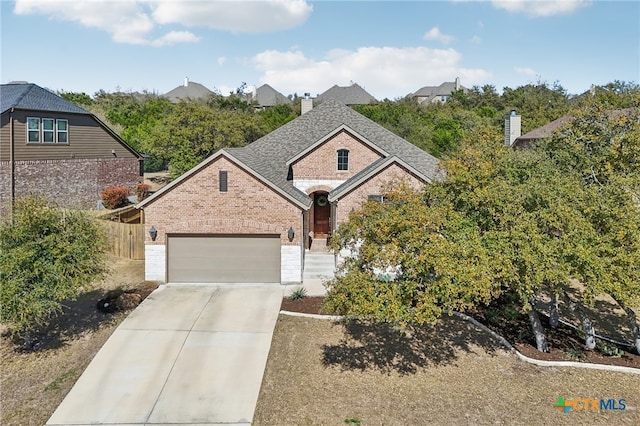 view of front of home with driveway, an attached garage, a shingled roof, brick siding, and a chimney