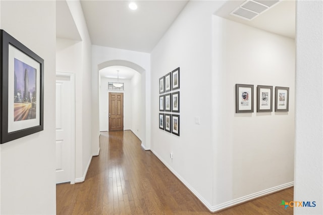 hall featuring visible vents, arched walkways, baseboards, and hardwood / wood-style flooring