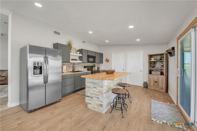 kitchen with black appliances, gray cabinetry, sink, a breakfast bar area, and a center island