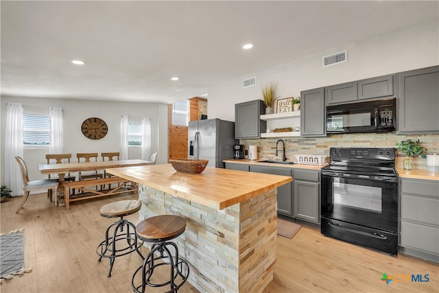 kitchen featuring sink, black appliances, a kitchen bar, gray cabinetry, and light wood-type flooring