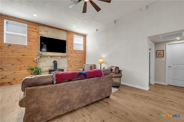 living room featuring wood walls, ceiling fan, light hardwood / wood-style flooring, and a wood stove