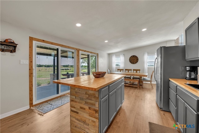 kitchen featuring stainless steel fridge, wood counters, gray cabinets, light hardwood / wood-style flooring, and a center island