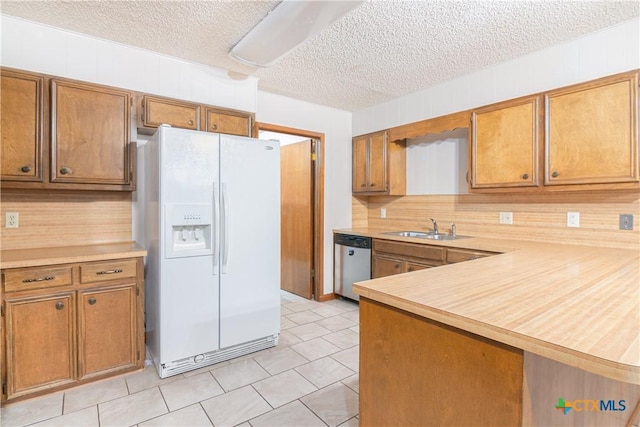 kitchen featuring brown cabinets, light countertops, stainless steel dishwasher, a sink, and white fridge with ice dispenser