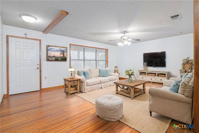 living room featuring a textured ceiling, hardwood / wood-style flooring, visible vents, baseboards, and a ceiling fan