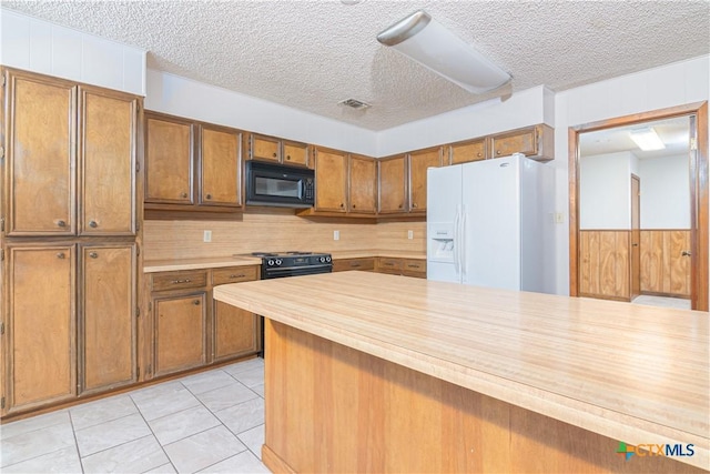 kitchen featuring wooden walls, light tile patterned floors, a textured ceiling, and black appliances